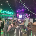 Tłum ludzi na Śląskim Festiwalu Nauki w Katowicach; widoczne stoisko Lasów Państwowych, dekoracje z zielonymi girlandami, duży neon ‘KATOWICE’ na podwyższonej platformie, sceny z ekranami i kolorowym oświetleniem.
